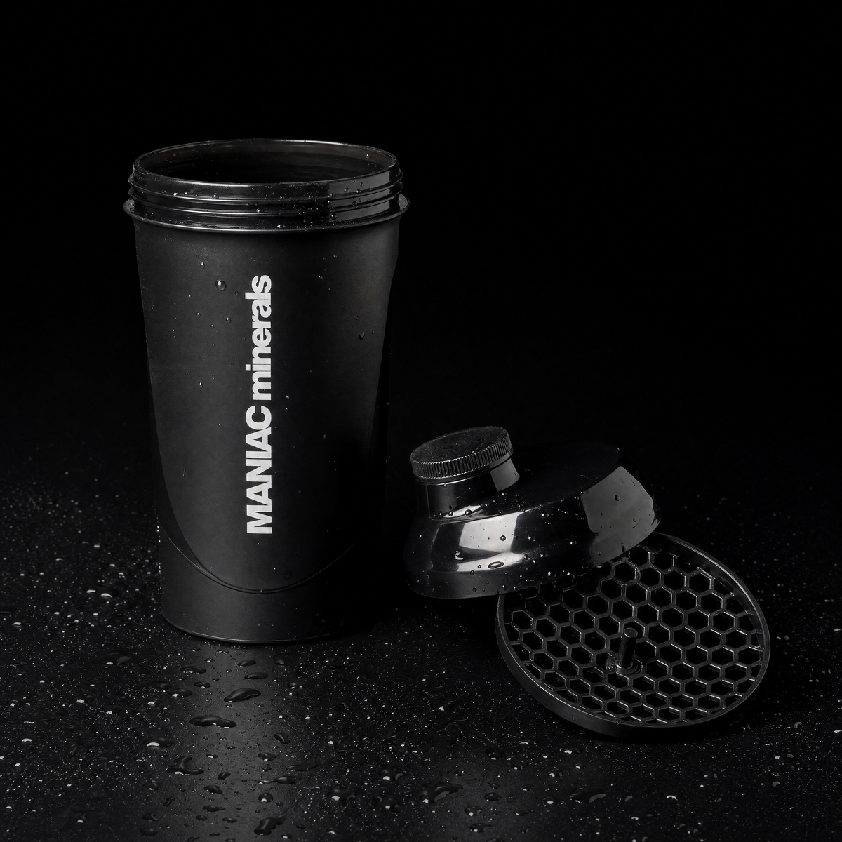 MANIAC Shaker 700 ml zerlegt: offene Flasche, Schraubdeckel mit Trinköffnung und herausgenommenes Wabensieb auf schwarzem Untergrund